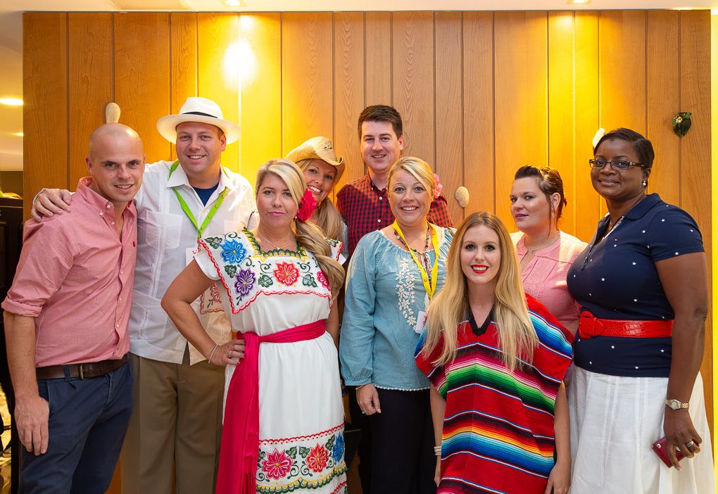 A large group of people stand in a row wearing colorful attire at what appears to be a social gathering or event.