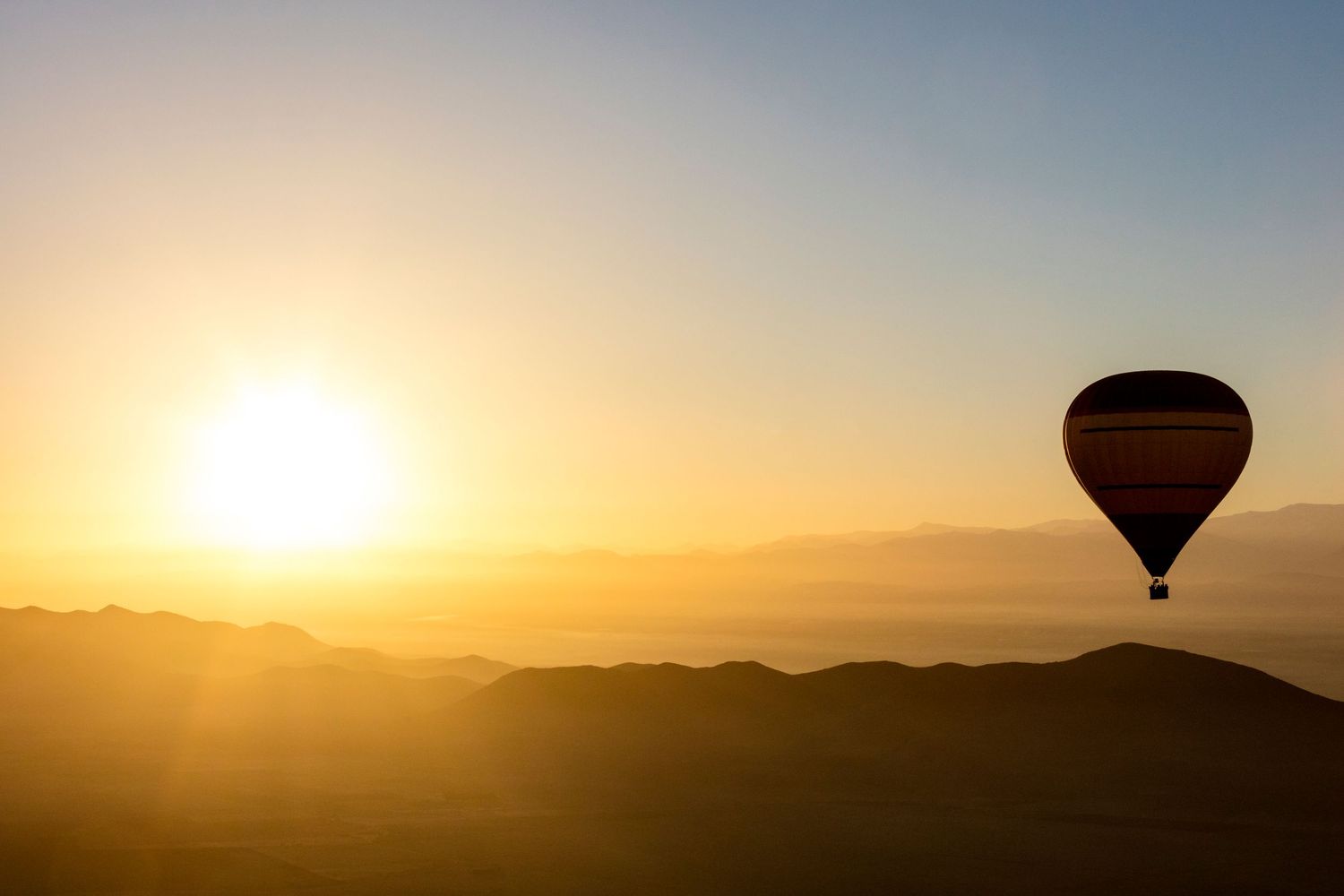 Hot air balloon silhouette floating over misty mountains during a golden sunrise in a serene landscape.
