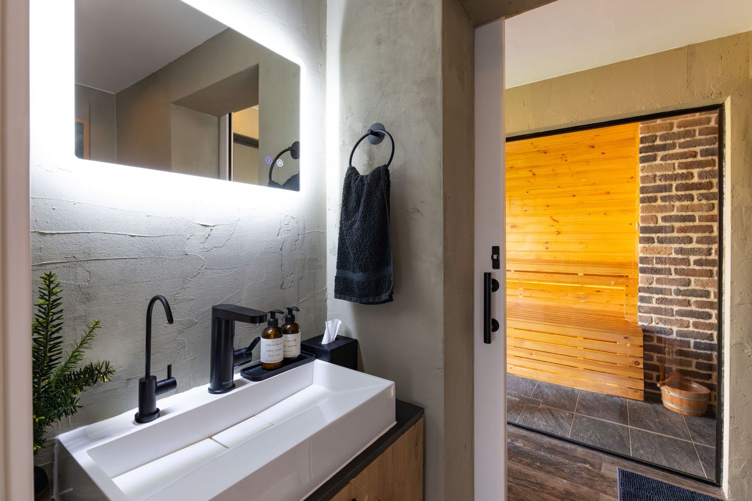 Modern spa bathroom in Bedfordshire with white vessel sink, matte black fittings and view into wood-panelled sauna.