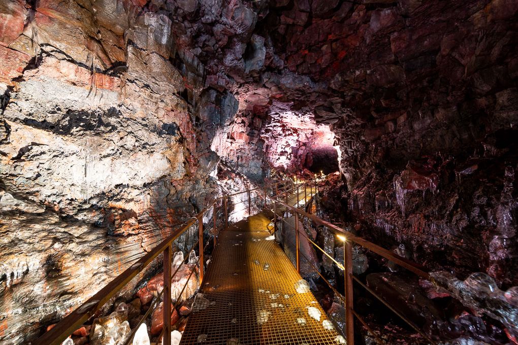 A series of dimly lit Icelandic lava tunnels at Raufarhólshellir. With rugged rock formations and walkways illuminated by warm lighting.