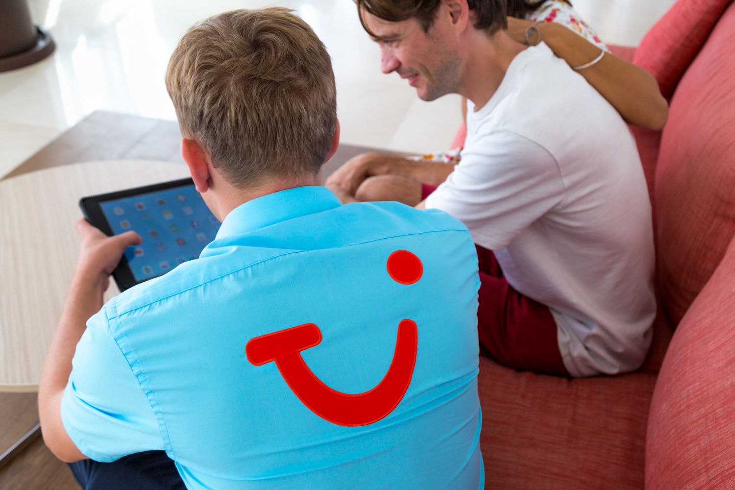 Two people sit together on a couch while wearing clothing with TUI Smile logo and looking at a device.