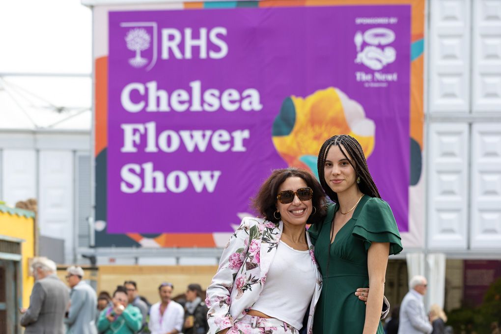 People walking past purple RHS banners and signage at the Chelsea Flower Show entrance.