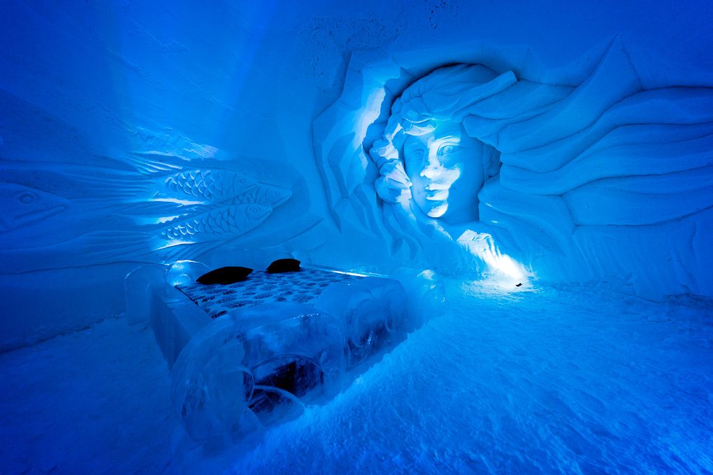 Illuminated blue ice cave with carved walls and tunnels glowing ethereally in Lapland, Finland. Ice Village excursion photography.
