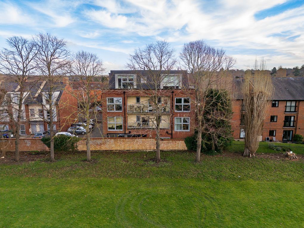 Aerial property photography of a brick residential building with dormers and bare trees against a bright blue cloudy sky.
