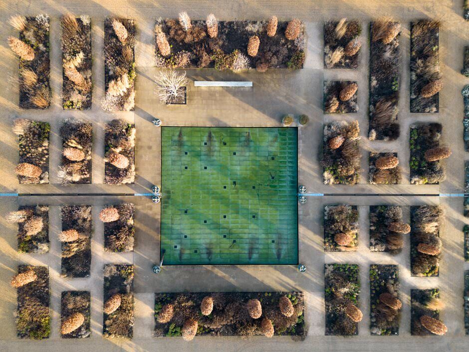 Aerial view of residential neighborhoods with green fields and geometric patterns of houses and trees seen from above.