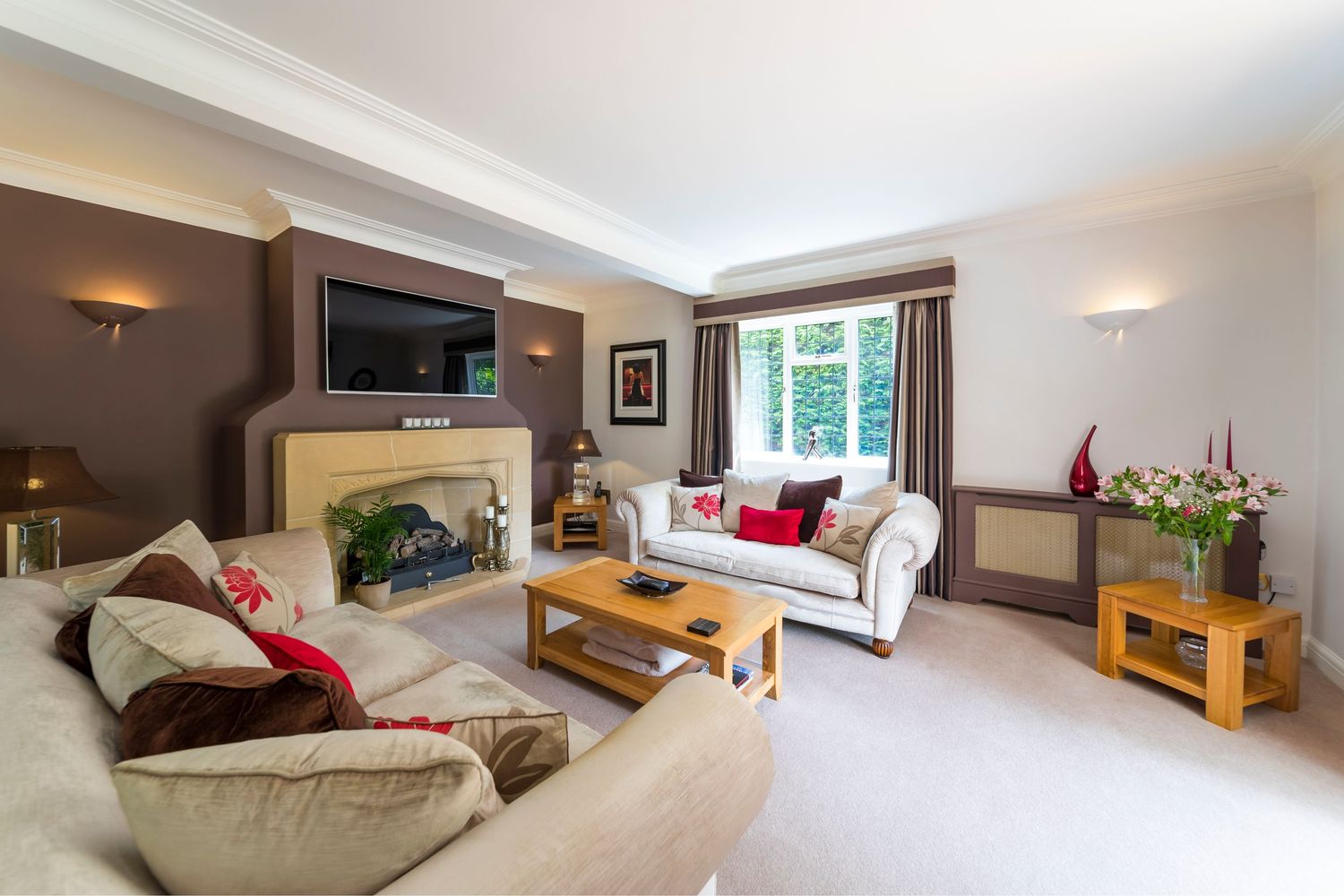 Elegant living room with cream sofas, fireplace, wall-mounted TV, wooden coffee table, and large window with garden views.