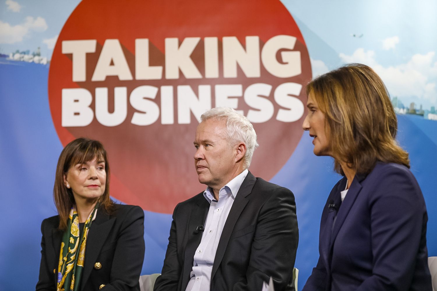 Three business professionals engaged in discussion at a Talking Business panel event on stage.