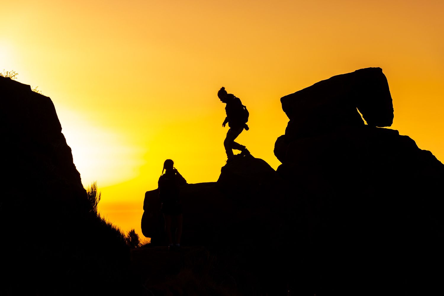 Silhouette of a figure hiking on rocky terrain against a vibrant golden sunset sky.