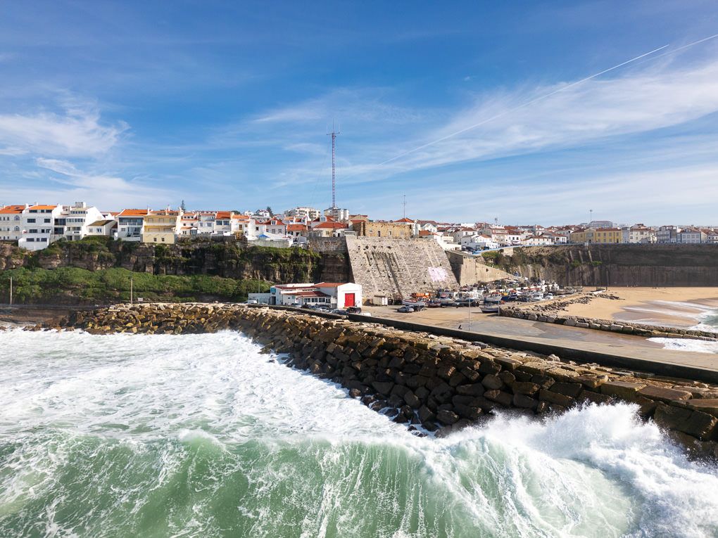 Rocky coastal landscape with ocean waves crashing against a breakwater under blue skies in Porto, Portugal.