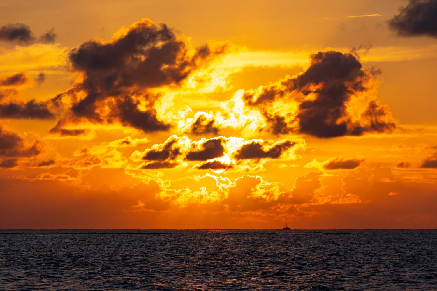 Dramatic orange sunset over dark ocean waters with sunlight breaking through cloudy skies.