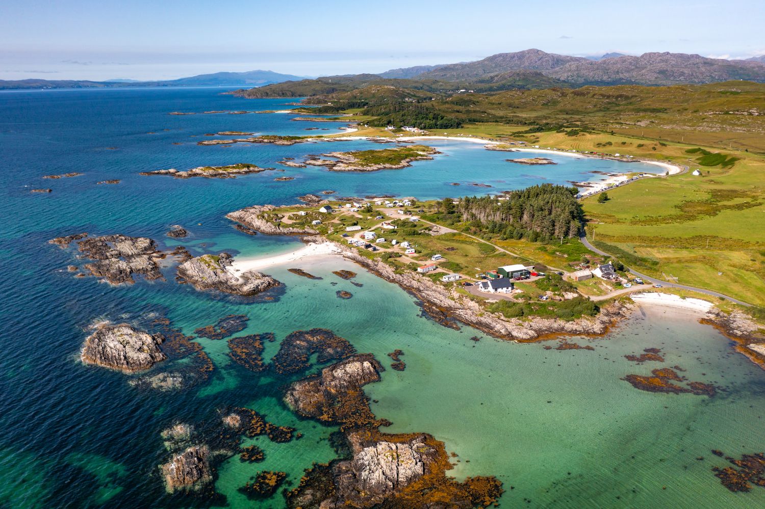 Aerial view of rugged Scottish coastline with turquoise waters, rocky cliffs and sandy beaches along the scenic shore.