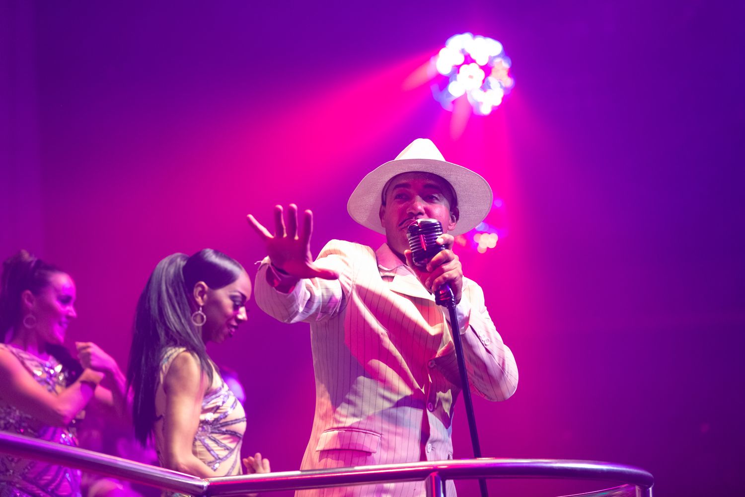 Performers on stage at a concert with vibrant purple and pink lighting, creating an energetic atmosphere.