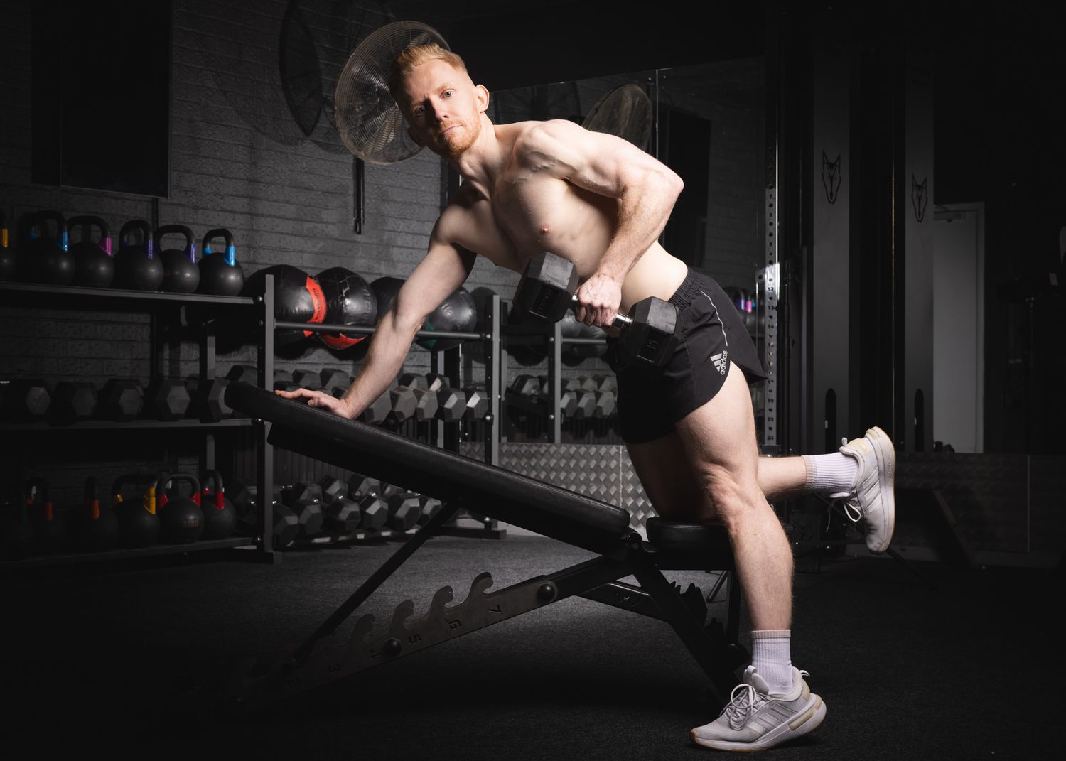 Athletic person performing a single-arm dumbbell row exercise in a dark gym setting with weights visible in background.