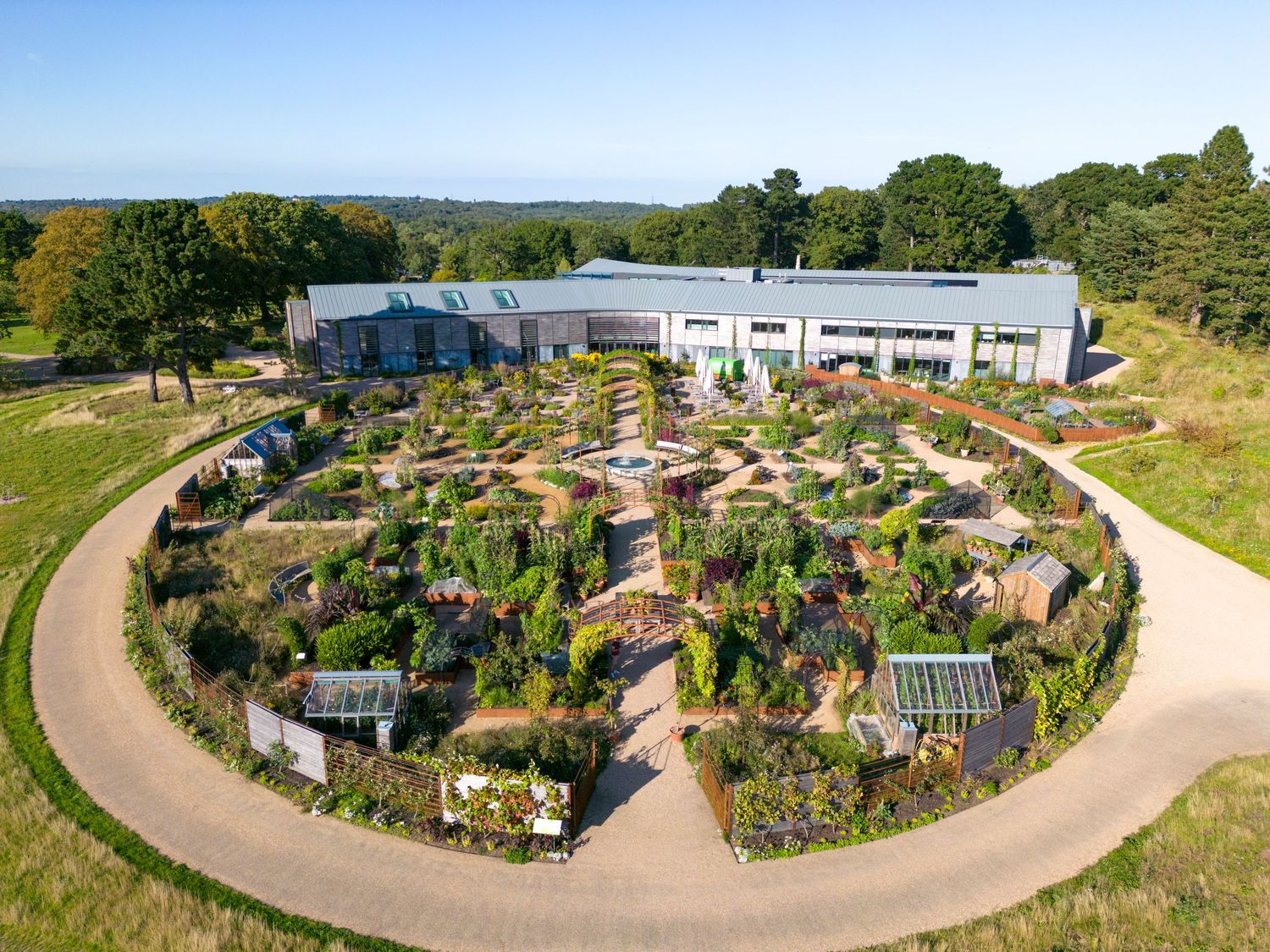 Aerial drone photograph of a circular garden design featuring diverse planting, winding pathways and a contemporary greenhouse.