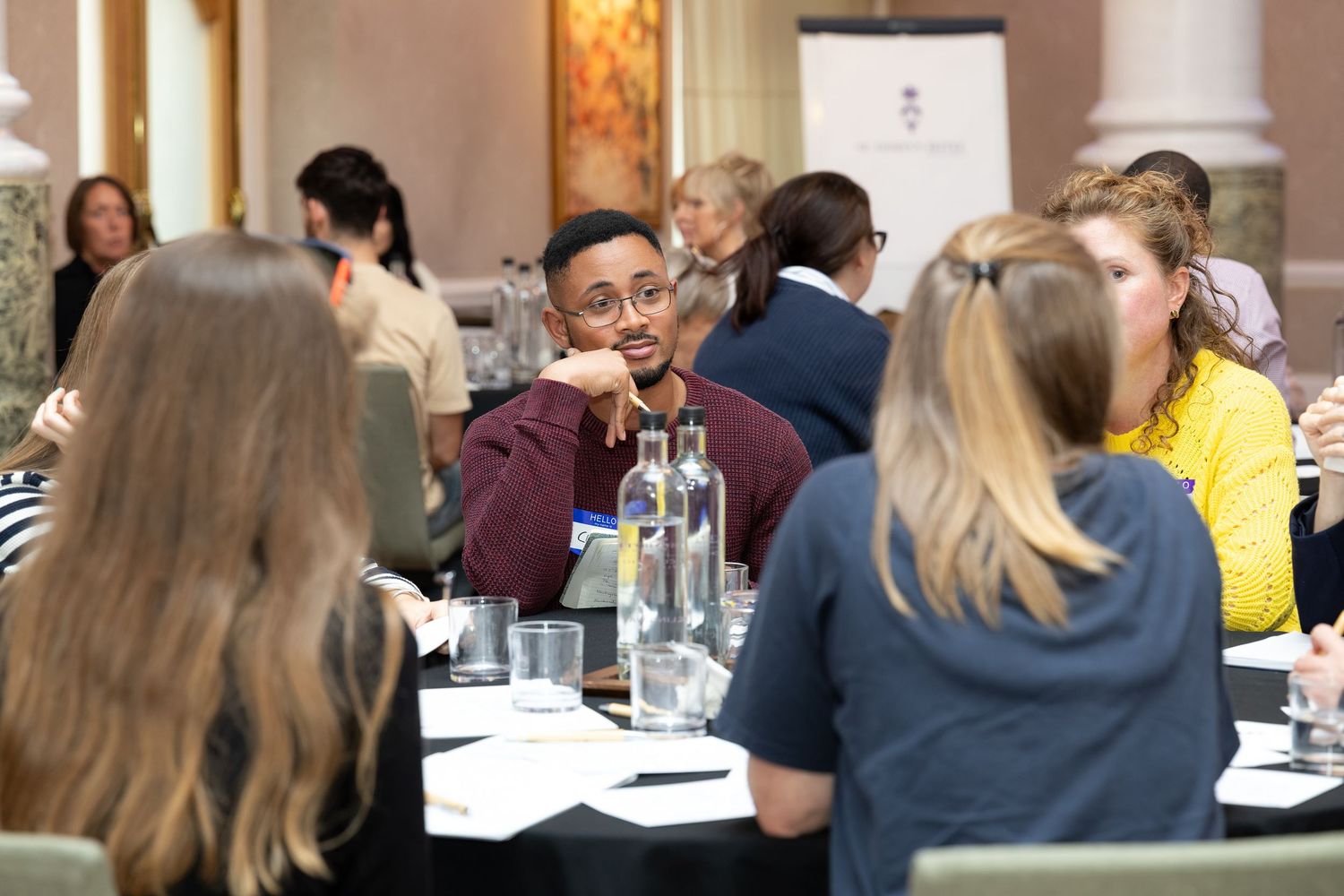 Diverse group of professionals engaged in discussion at round tables during a business networking event.