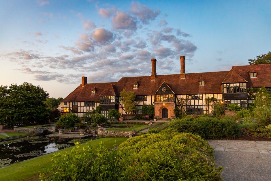 Modern glass building nestled in a landscaped garden with winding paths and flowering plants at sunset.