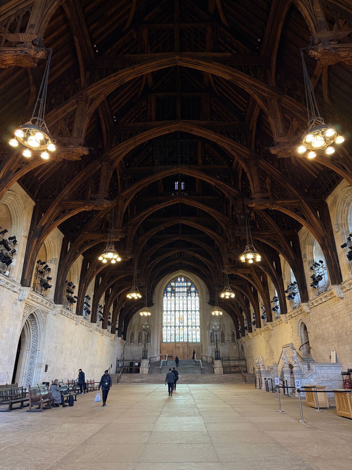 Interior view of Westminster Hall's grand medieval architecture with vaulted wooden ceiling and hanging chandeliers.