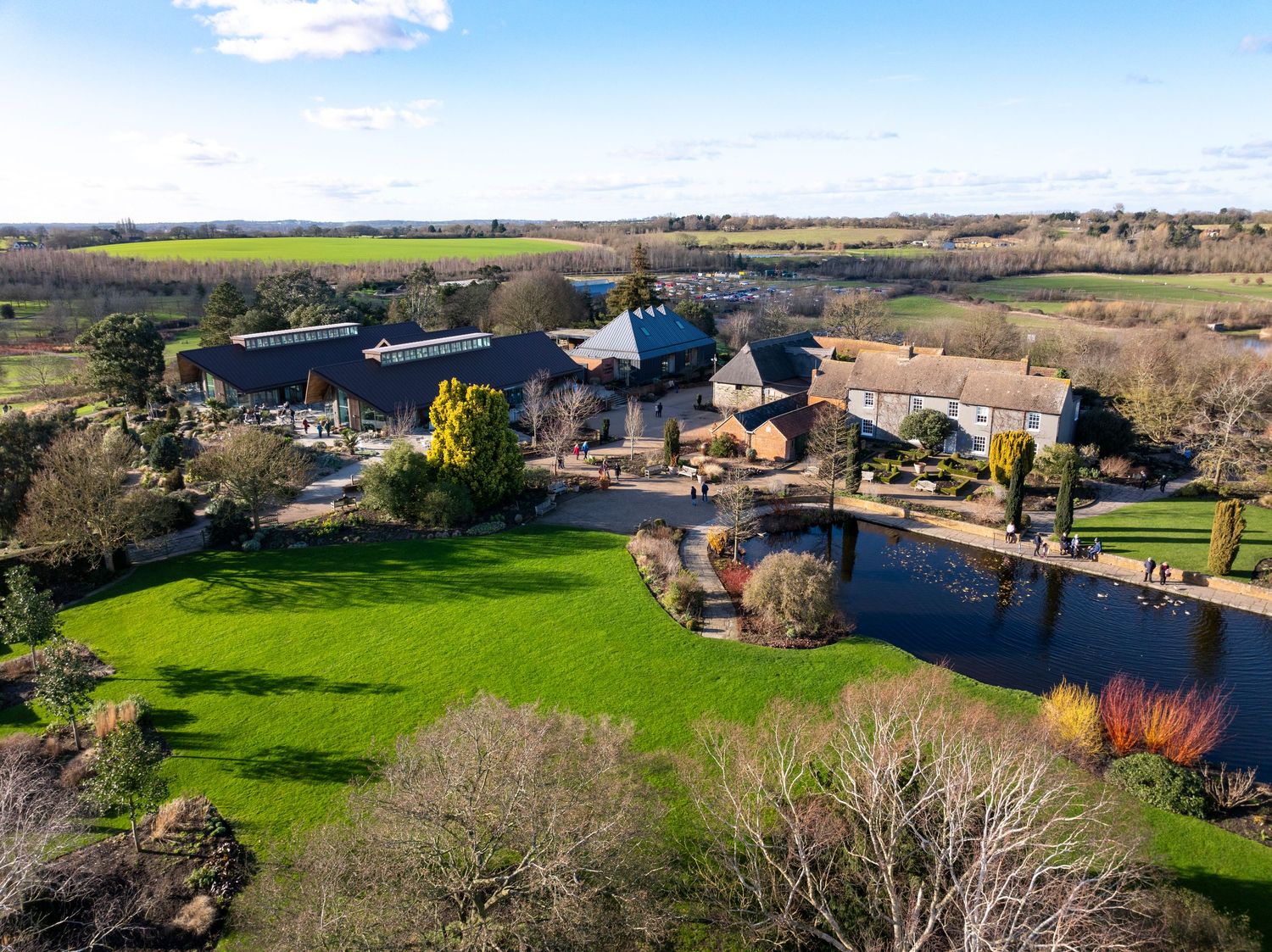 Aerial drone photograph of a historic country estate featuring landscaped gardens, a private lake and surrounding farmland.