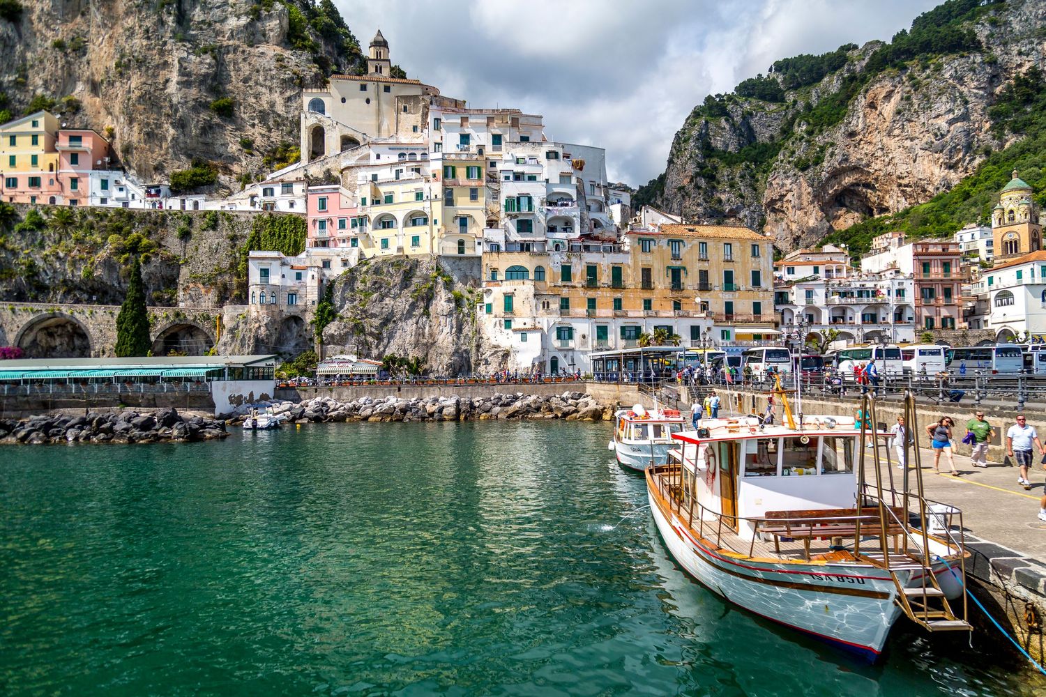 Colorful buildings cascade down cliffs to a harbor with boats in Amalfi, Italy.