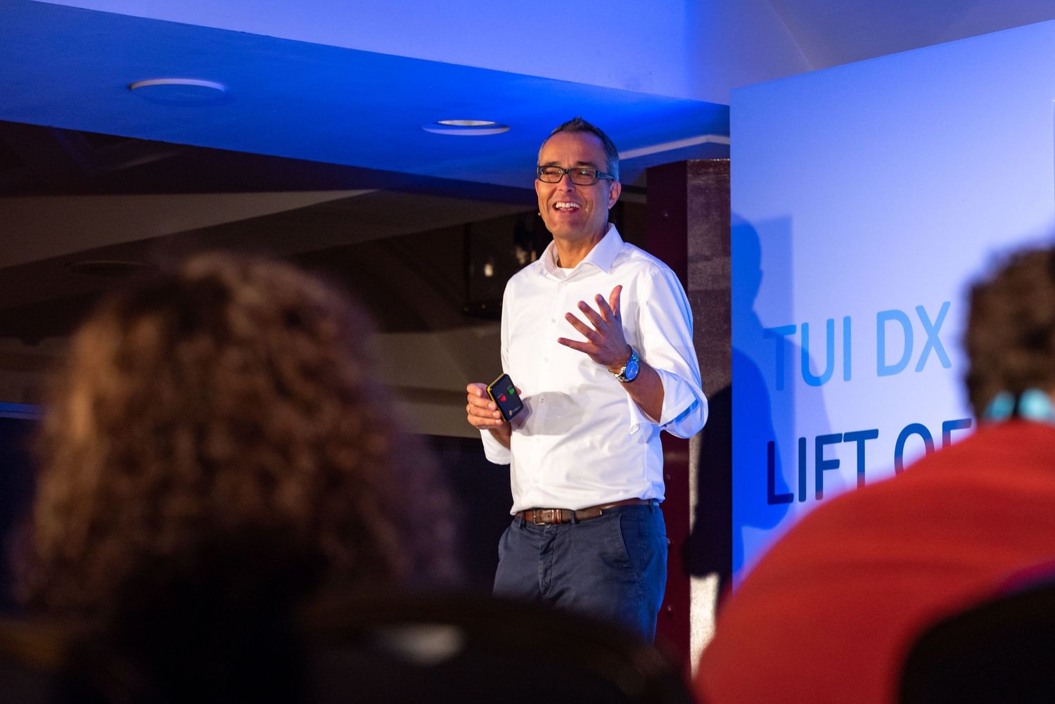 Speaker presenting at TUI DX Lift Off event, gesturing on stage before an audience in a blue-lit venue.