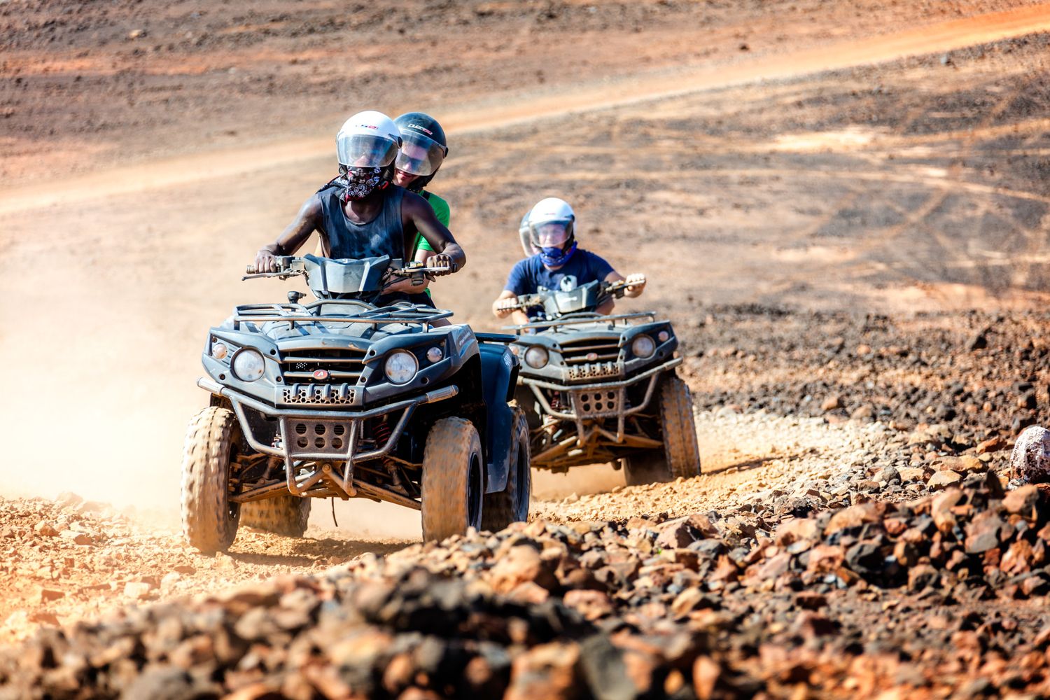 Two ATVs racing through dusty desert terrain with riders wearing protective gear and helmets.