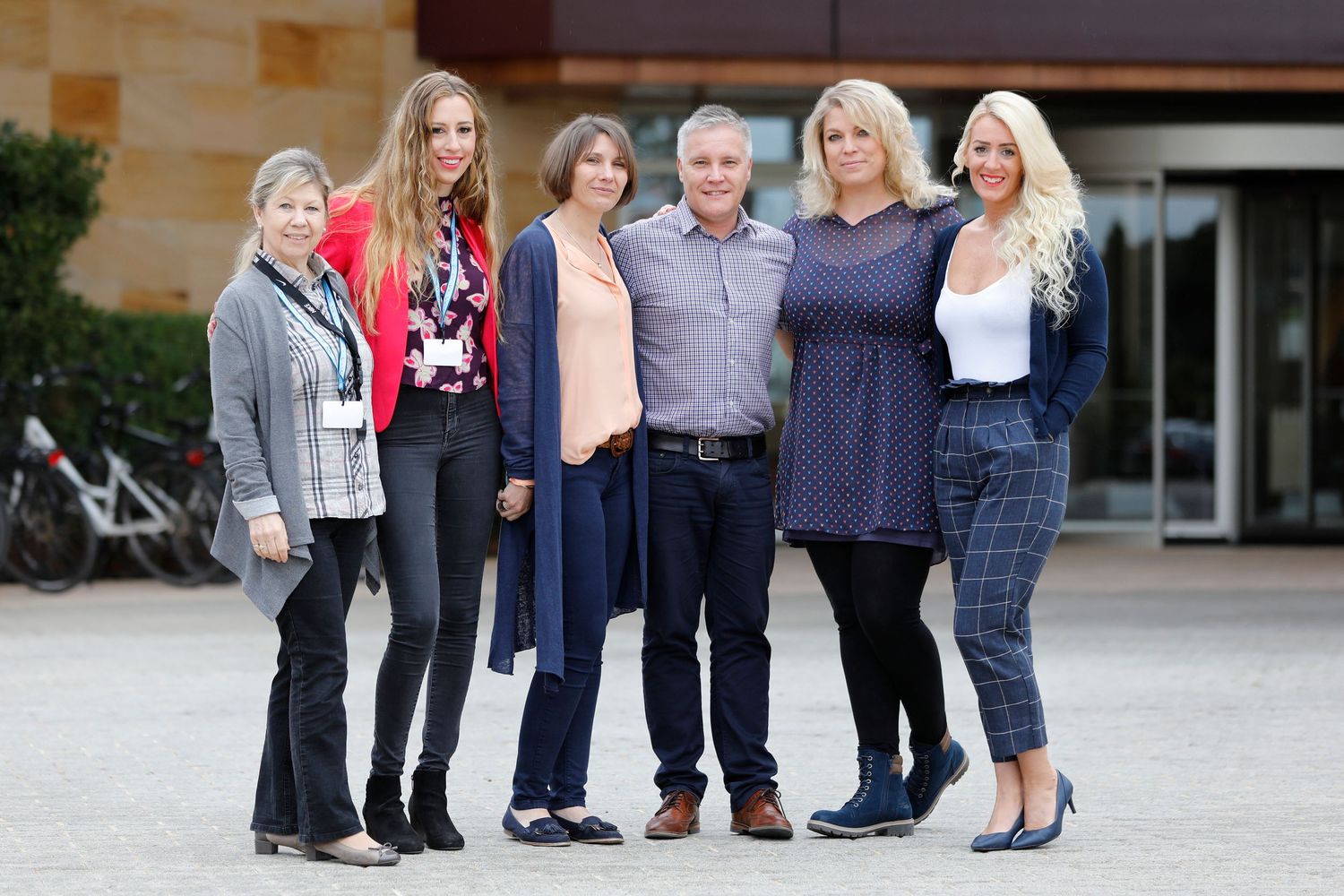 Group of six adults posing together outdoors near a modern building, smiling for a group photo.