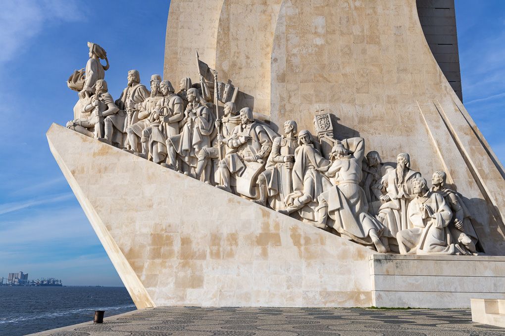The Monument of Discoveries in Lisbon, Portugal features detailed stone carvings along its sides against a blue sky.