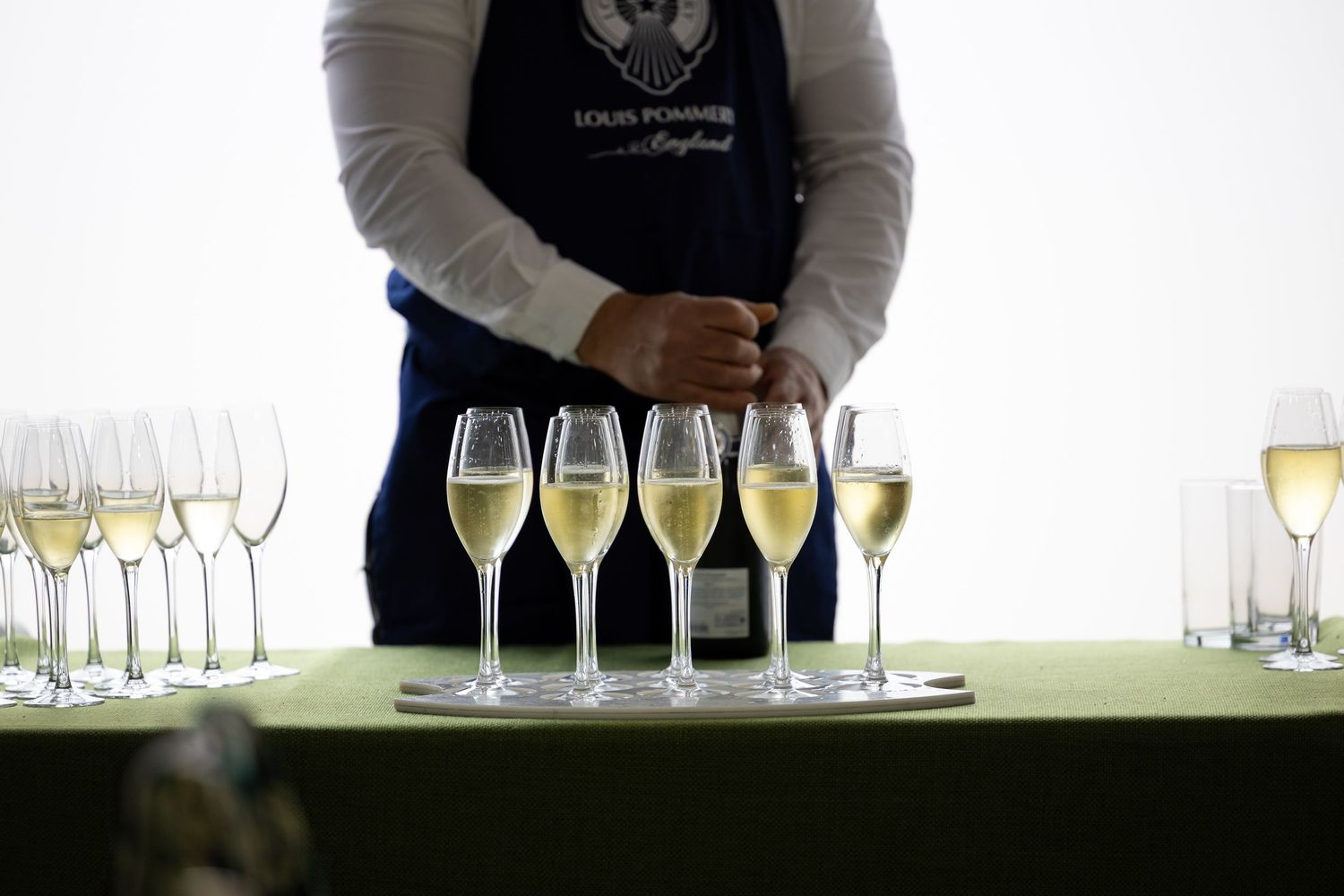 Waiter in Louis Pommery apron pouring champagne into elegant flute glasses at a formal tasting event.