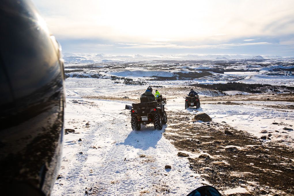 A point of view excursion photo of ATVs in a snowy winter landscape with rugged terrain and dramatic cloudy sky over a barren wilderness.