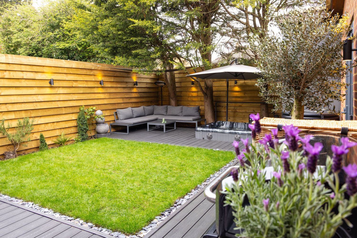 Garden spa in Bedfordshire with landscaped lawn, outdoor seating area, wooden fencing and purple flowers on decking.