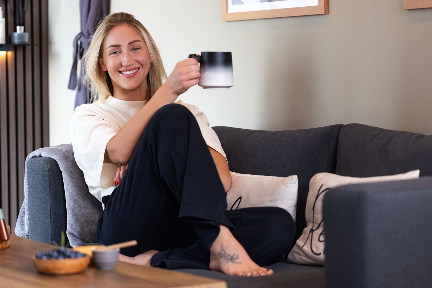 Woman relaxing on sofa in Bedfordshire spa lounge, holding mug, captured during lifestyle interior photography shoot.