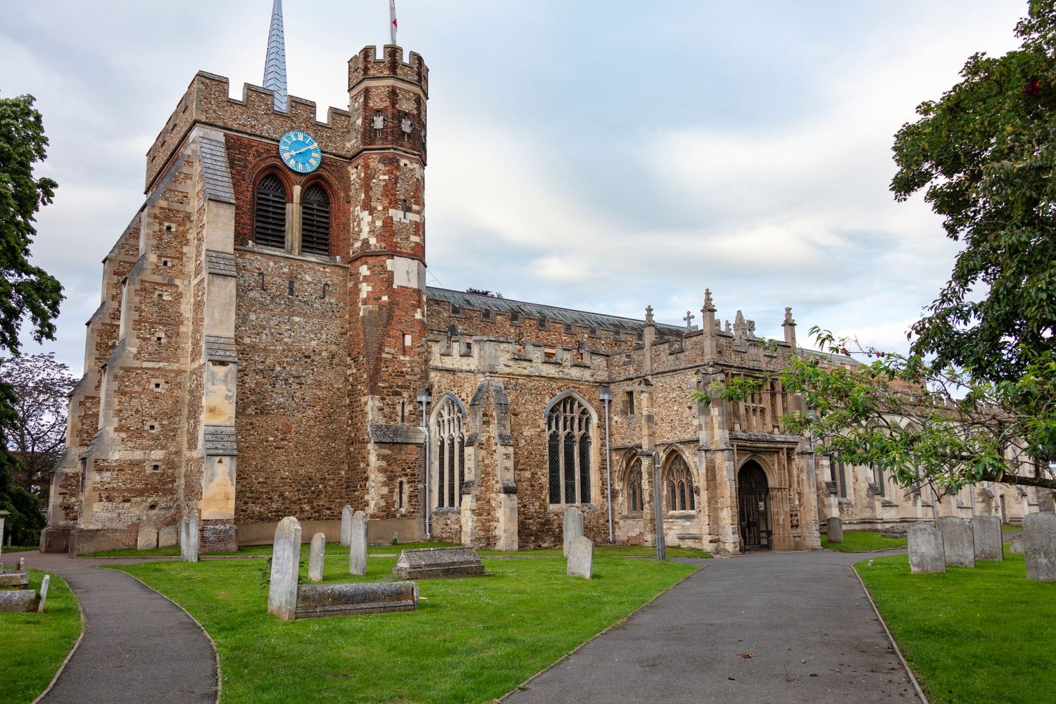 Historic medieval stone church with tower surrounded by grassy churchyard and gravestones on a cloudy day in England.