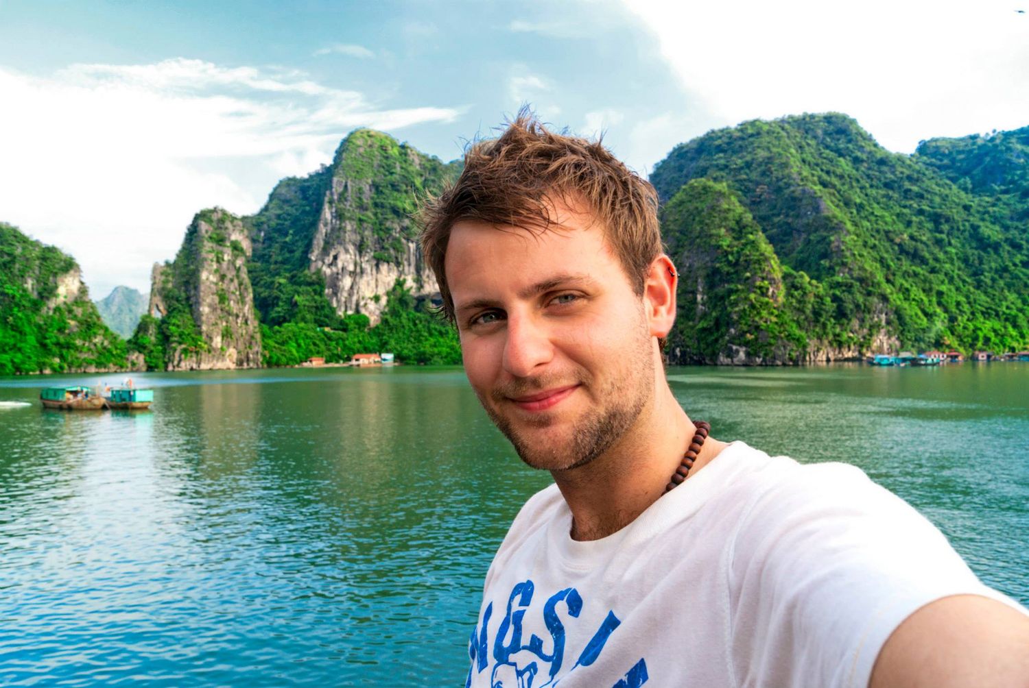 Tourist takes selfie photo at Ha Long Bay in Vietnam with scenic limestone karst mountains and blue water in background.