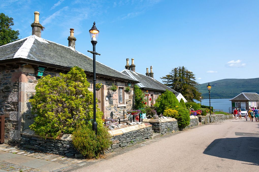 Traditional stone cottages along a scenic path in Loch Lomond, Scotland, with vintage lampposts and mountain views.