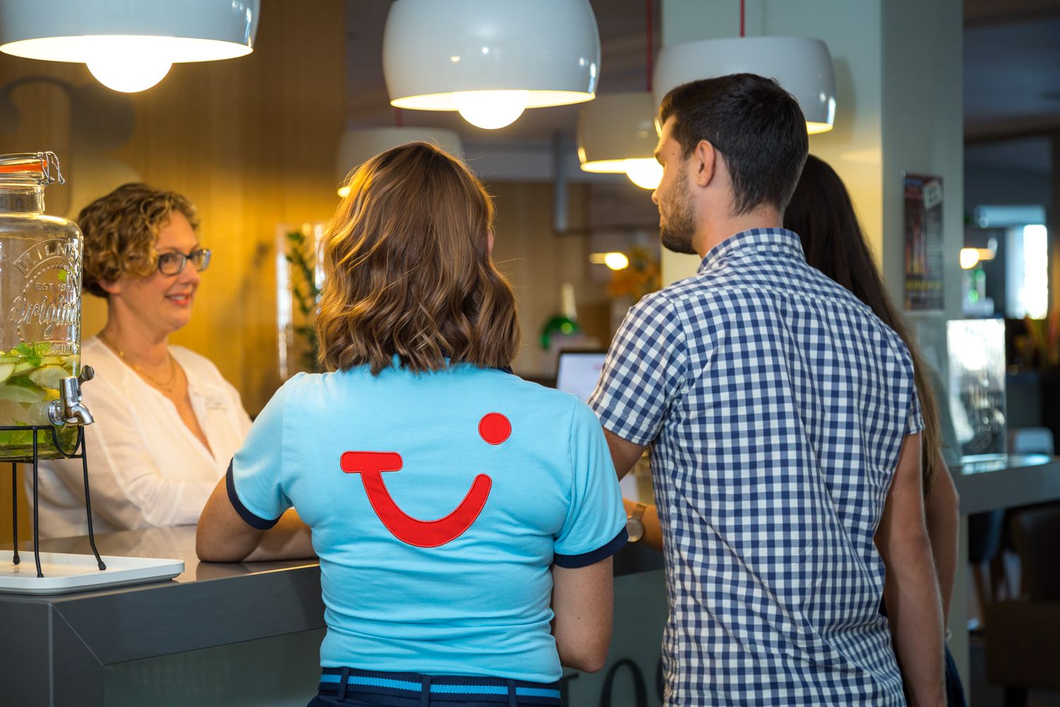 Three people stand at a counter, with one wearing a bright blue TUI Smile logo shirt in a casual indoor setting.