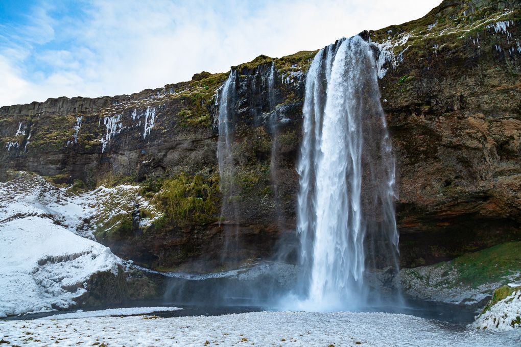 Majestic Seljalandsfoss waterfall cascades down moss-covered cliffs in southern Iceland on a bright sunny day.