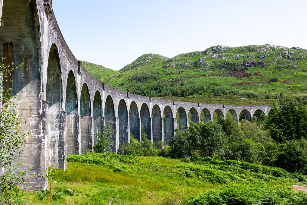 The historic Glenfinnan Viaduct railway bridge stretches across a scenic valley in the Scottish Highlands.