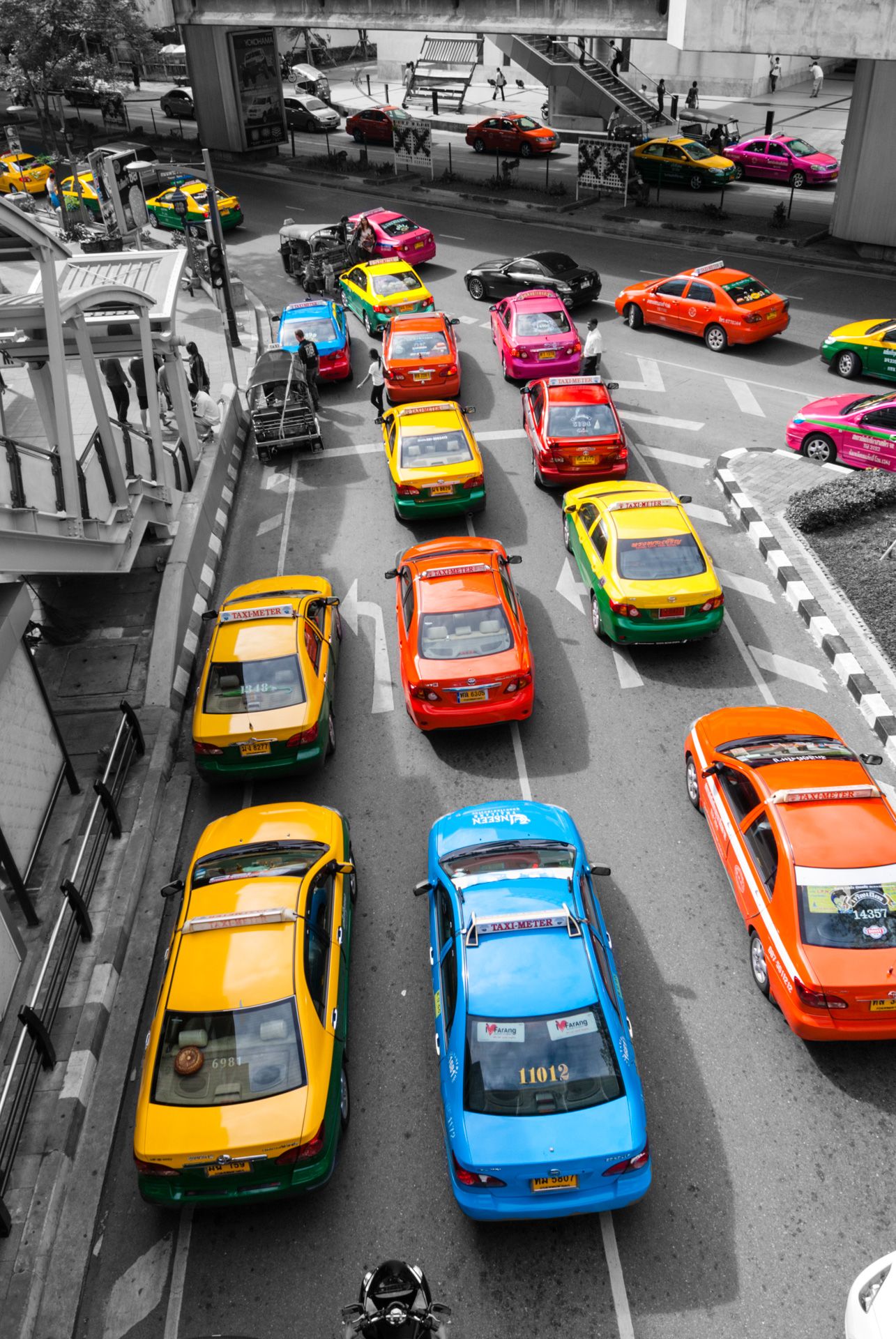 Colorful taxis lined up on a street with selective color highlighting the vibrant vehicles against a black and white background.