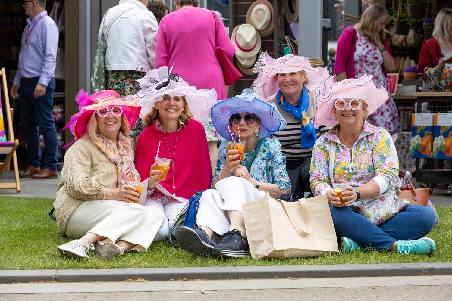 A group of people wearing pink and white outfits sit together on the grass during an outdoor event.