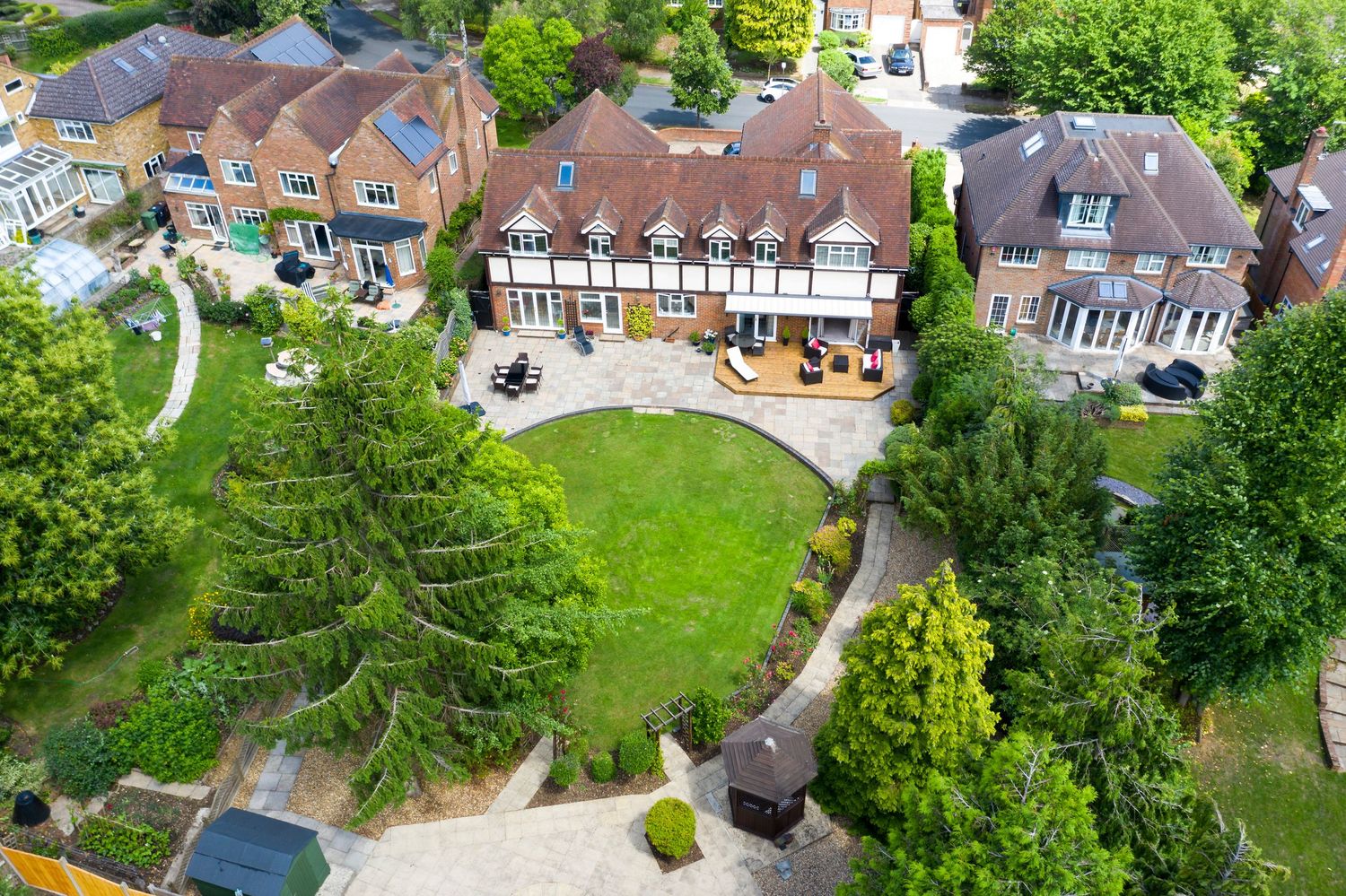Aerial view of luxury Tudor-style residence with landscaped grounds, mature trees and circular lawn.
