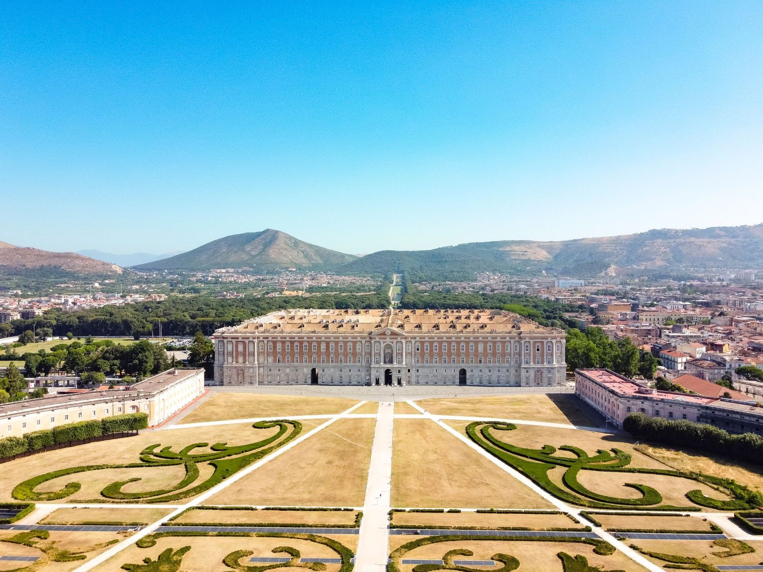 Aerial photography of the Royal Palace of Caserta showcasing formal gardens, historic architecture and surrounding landscape.