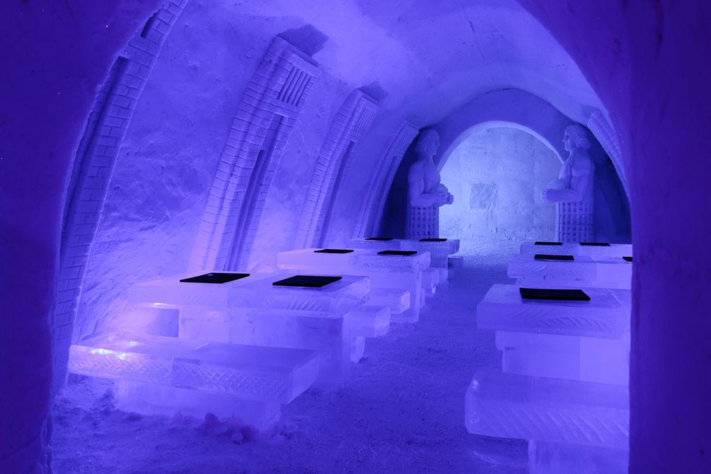 Glowing purple ice hotel interior with curved archways and illuminated walls creating a magical atmosphere. Ice Village excursion Lapland.