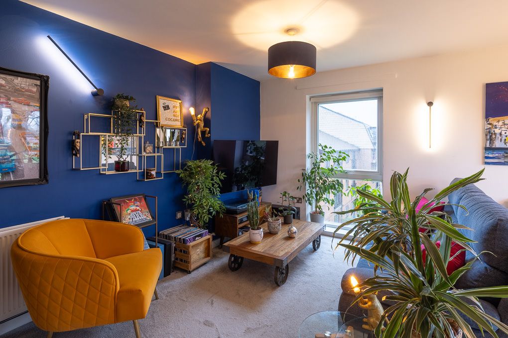 Real estate photography of a modern living room with a navy accent wall features an orange velvet armchair and houseplants.