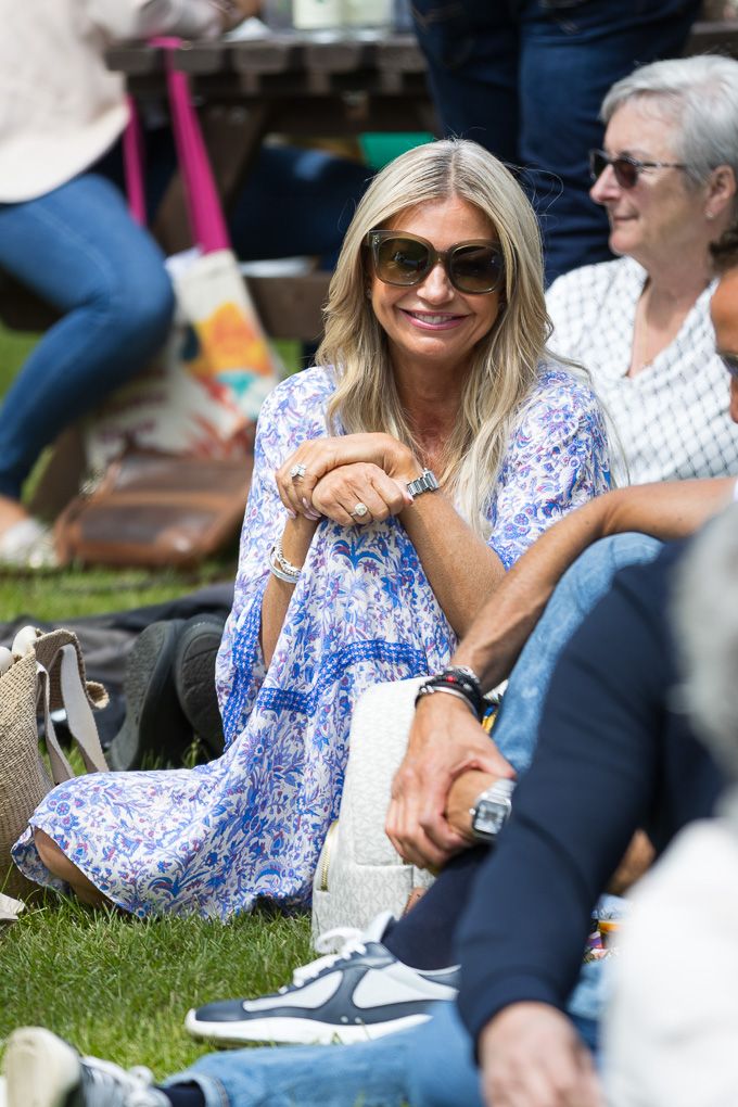 Woman in blue and white floral dress relaxes on grass during outdoor gathering wearing sunglasses.
