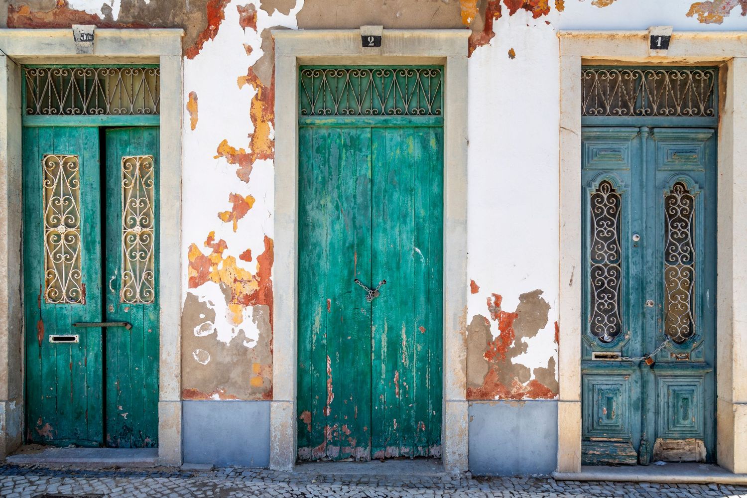 Three ornate antique turquoise doors on a weathered, peeling white facade of a historic Portuguese building.