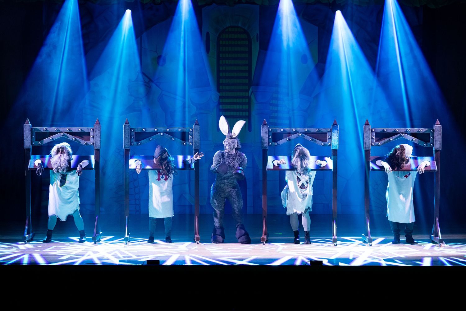 Theater performers in blue stage lighting with rabbit costume centerpiece and dramatic beam effects on stage.