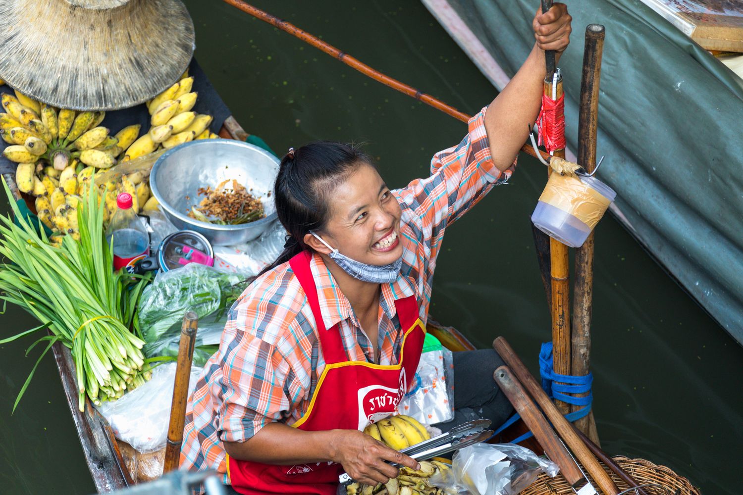 Food vendor preparing dishes at a traditional floating market in Thailand with fresh flowers and cooking ingredients nearby.