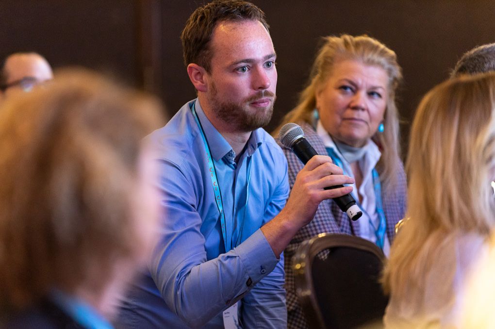 People sitting at tables in a dimly lit conference room engage in conversation during a TUI conference in London.