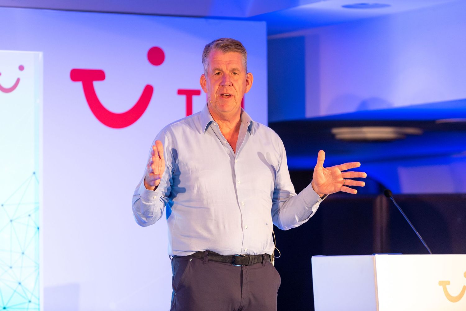Speaker presenting on stage at a TUI corporate conference with delegates and branded backdrop