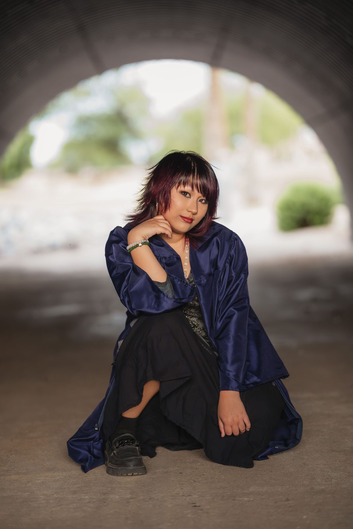 Woman in blue satin jacket and black skirt posing under stone arch outdoors.